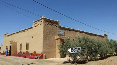 a large brick building with a sign in front of it at Hôtel Riad Tadarte Familier in Merzouga