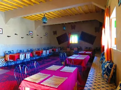 a dining room with red tables and blue chairs at Hôtel Riad Tadarte Familier in Merzouga