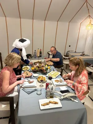 a group of people sitting at a table eating food at Desert Luxury Camp Merzouga in Merzouga