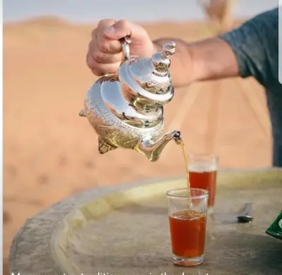 a person pouring a tea pot into a glass at MorokoTour Camp in Merzouga