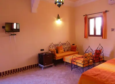 a bedroom with a bed and two chairs and a tv at Auberge La Source in Merzouga
