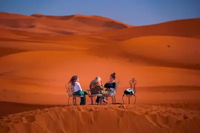 three people sitting in chairs on top of a desert at Kasbah Erg Chebbi in Merzouga