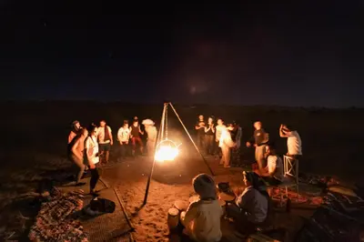 a group of people standing around a fire at night at Aiour Luxury Camp in Merzouga