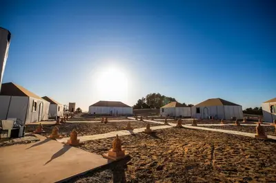a row of tents with the sun in the background at Aiour Luxury Camp in Merzouga
