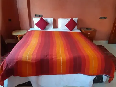 a large bed with a colorful striped blanket on it at Hôtel Restaurant Dar Al Madina in Tinerhir