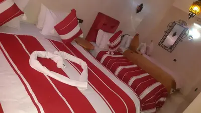 two beds in a hotel room with red and white stripes at Hôtel Restaurant Dar Al Madina in Tinerhir