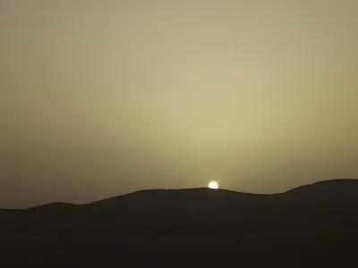 a sunset on a hill with the sun on the horizon at Sahara Desert Camp in Hassilabied