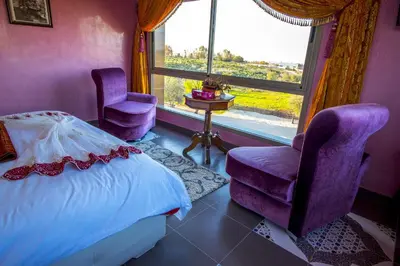 a bedroom with purple chairs and a bed and a window at Maison d'hôtes La Ferme AZIZA in Fès