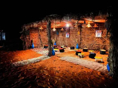 a room with a straw hut with trees and couches at Desert camp camel & sandboarding in Merzouga