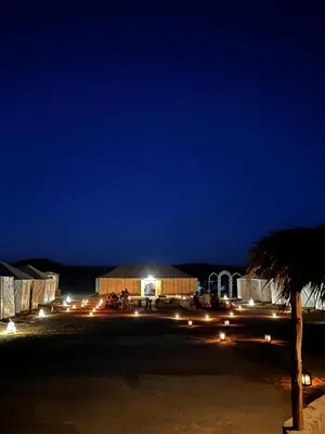 a building with lights at night with a palm tree at Camp atlantic chegaga in Mhamid