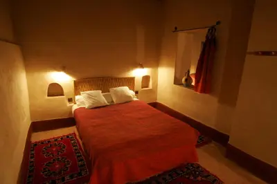 a bedroom with a bed with red sheets and white pillows at Gite Elkhorbat in Tinejdad