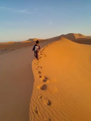 a man standing on a sand dune in the desert at Hotel Riad Ali in Merzouga