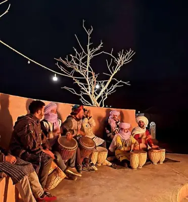 a group of people sitting on a wall at night at Hotel Riad Ali in Merzouga
