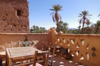 a table and chairs on a balcony with palm trees at Kasbah Maktob Tamnougalt in Agdz