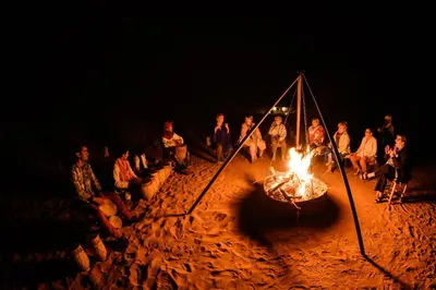 a group of people sitting around a fire in the sand at Desert Heart Luxury Camp in Merzouga