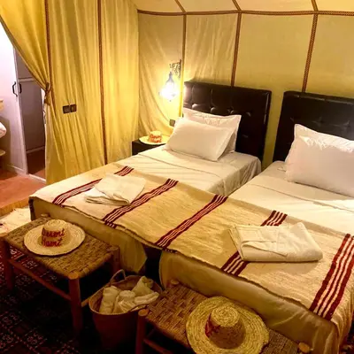 a bedroom with two beds and a table and chairs at Desert Heart Luxury Camp in Merzouga