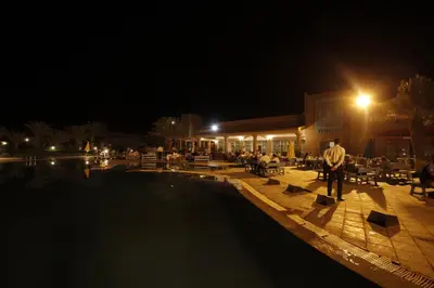 a man standing next to a swimming pool at night at Belere Arfoud in Erfoud