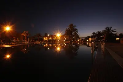 a swimming pool at night with palm trees and lights at Belere Arfoud in Erfoud