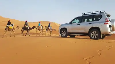 a group of people riding camels in the desert at Visit Morocco Sahara Camp in Merzouga