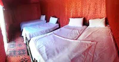 three beds in a room with red walls at Visit Morocco Sahara Camp in Merzouga