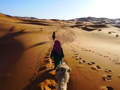 a person walking in the desert with a camel at Visit Morocco Sahara Camp in Merzouga