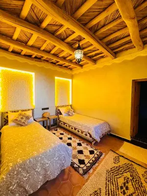 a yellow room with two beds and a wooden ceiling at Hiking Nomads Guesthouse in Tamellalt
