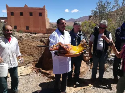 a man holding a turkey on a plate with people at Auberge Camping BOUGAFER Tamtetoucht in Tamtetoucht