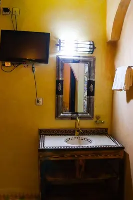 a bathroom sink with a mirror on a yellow wall at Dar Diafa Kaltom in Ouzoud