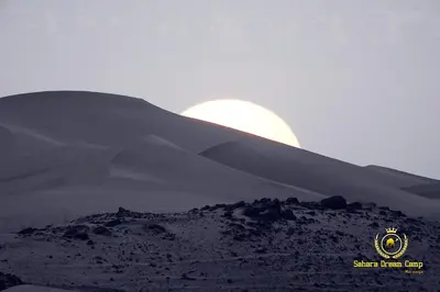 a moonrise over a sand dune with the sun in the background at Luxury Sahara Dream Camp in Merzouga