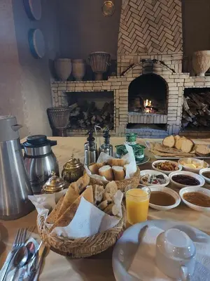 a table with baskets of bread and a fireplace at Maison Merzouga Guest House in Merzouga