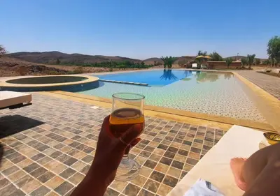 a person holding a glass of beer in front of a swimming pool at Kasbah Zitoune in Ouarzazate