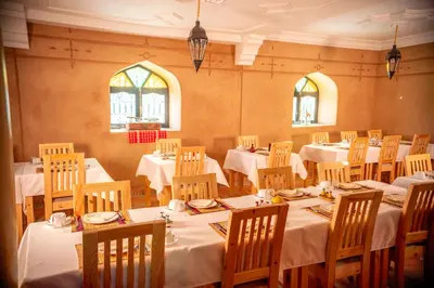 a dining room with white tables and chairs and windows at Kasbah Zitoune in Ouarzazate