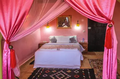 a bedroom with a large bed with pink curtains at Taloute Ecolodge in Skoura
