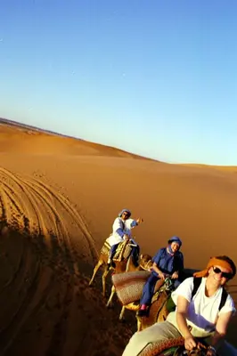 three people riding on camels in the desert at Haven La Chance Desert Hotel in Merzouga