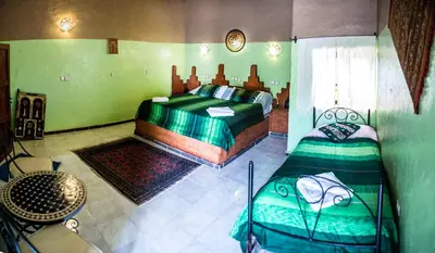 a bedroom with two beds and a table in it at Haven La Chance Desert Hotel in Merzouga