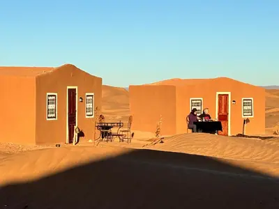 a group of people sitting in front of a building in the desert at Bivouac La Dune Blanche in Mhamid