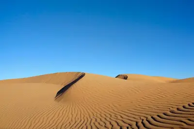 a camel sitting on a sand dune in the desert at Bivouac La Dune Blanche in Mhamid
