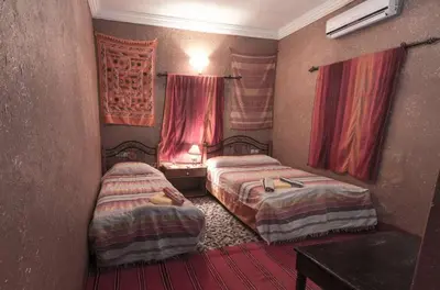 two beds in a small room with red curtains at Kasbah Valentine in Aït Ben Haddou