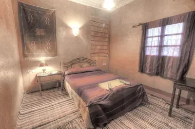 a bedroom with a bed and a table and a window at Kasbah Valentine in Aït Ben Haddou
