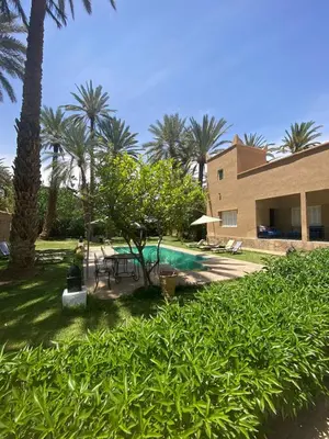 a backyard with a pool and palm trees and a building at Maison d Hôte Ighrem in Goulmima