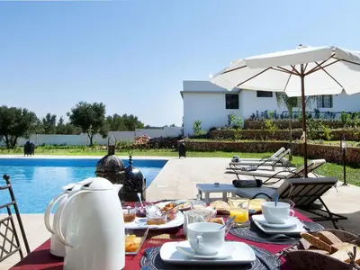 a table with food and an umbrella next to a pool at Villa Agapanthe in Fès