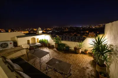 a rooftop patio with tables and potted plants at night at Le Cèdre D'argent in Fès