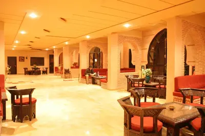 a lobby with tables and chairs and a man sitting on a couch at Hôtel LAKASBAH Ait Ben Haddou in Aït Ben Haddou