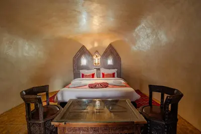 a bedroom with a bed with a table and chairs at Kasbah Tizzarouine in Boumalne
