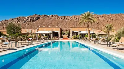 a swimming pool with chairs and a mountain in the background at Hotel Bab Rimal - Your Foum Zguid Escape in Foum Zguid