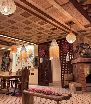 a room with a table and a fireplace and chandeliers at Gîte d'étape Tamaloute in Bou Tharar