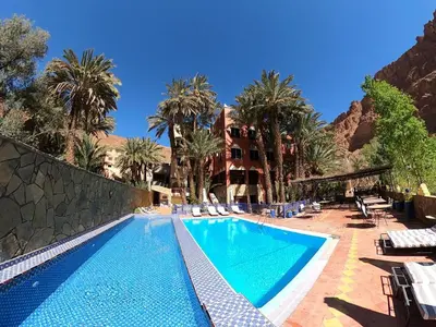 a swimming pool with palm trees and a building at Kasbah Restaurant Amazir in Tinerhir