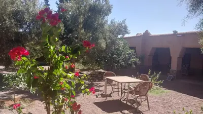 a table and chairs in a yard with red roses at Kasbah Auberge Bassou in Nkob