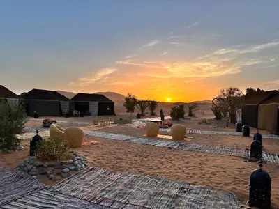 a sunset in the desert with a group of tents at Sahara wellness camp in Merzouga