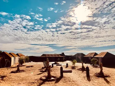 a group of tents in the desert under a cloudy sky at Sahara wellness camp in Merzouga